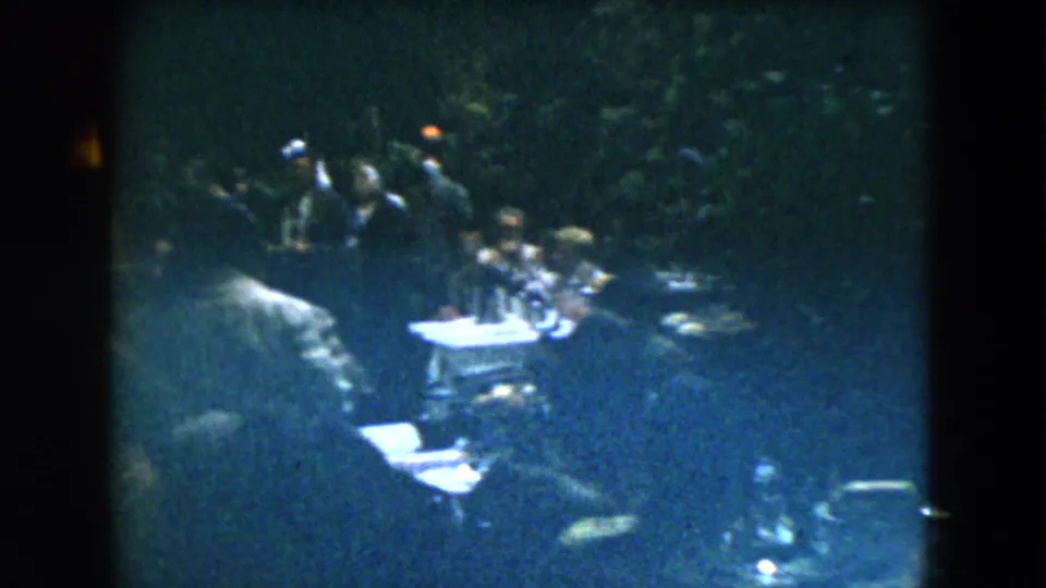 1962 Mexico City 8mm frame showing adults seated at restaurant tables under very dim lighting and deep shadows.