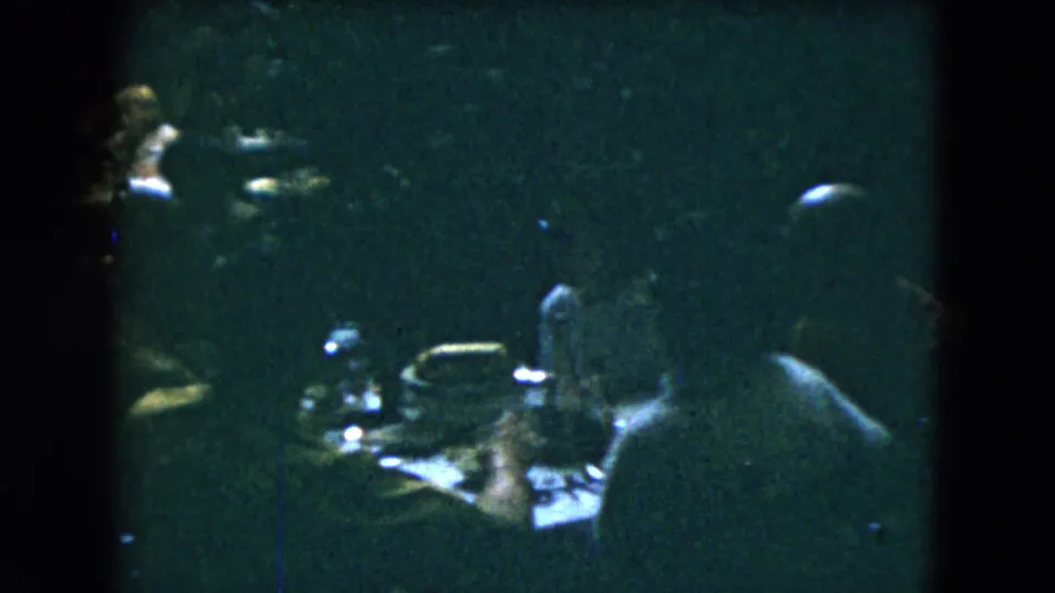 1962 Mexico City restaurant scene with silhouettes of diners, tableware, and scattered highlights in low-exposure 8mm footage.