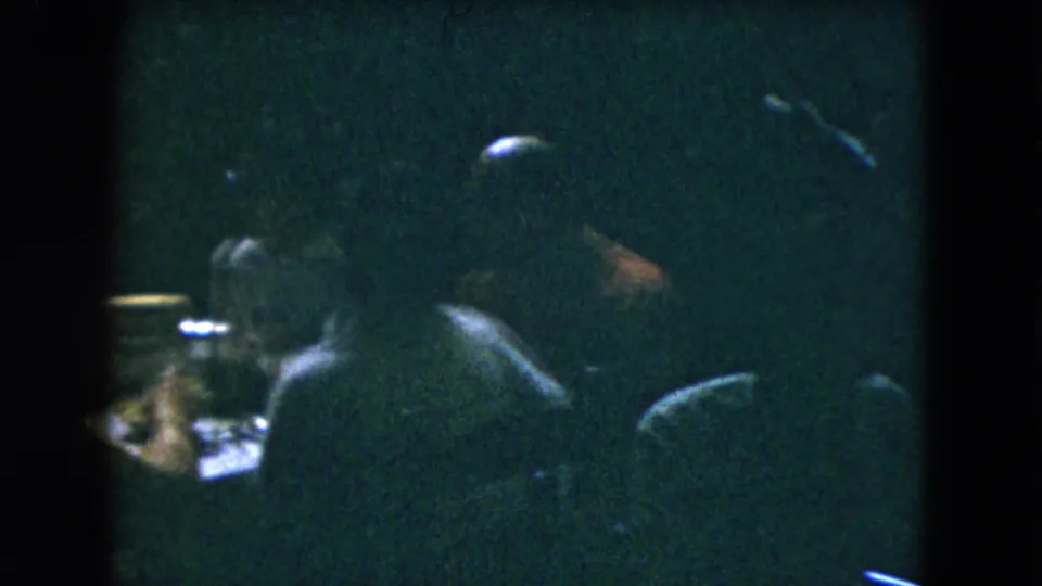 1962 Mexico City 8mm frame showing a seated foreground patron and nearby dining tables in heavy shadow.