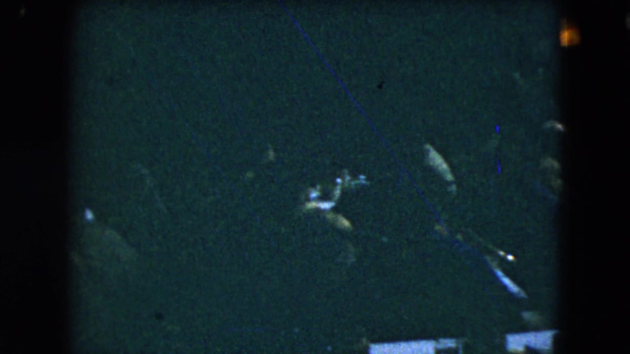 Mexico City 1962 home-movie frame showing dark silhouettes of guests around tables in a crowded indoor gathering.