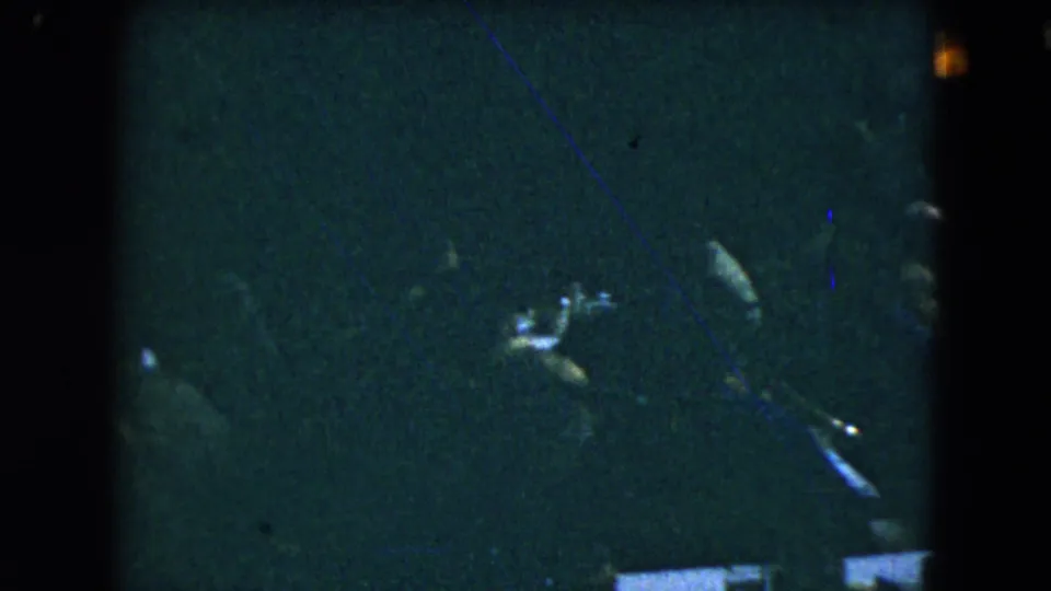 Mexico City 1962 home-movie frame showing dark silhouettes of guests around tables in a crowded indoor gathering.