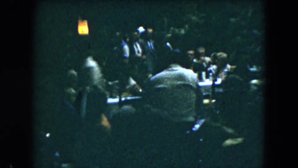 Mexico City 1962 home-movie frame showing a crowded indoor table scene with guests eating or talking under low light.
