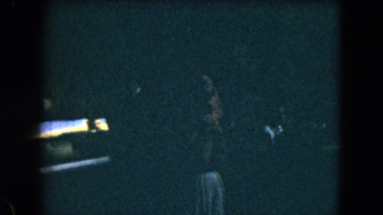 1962 Mexico City home-movie frame showing a partially visible person in a dim interior, with heavy grain and low exposure.
