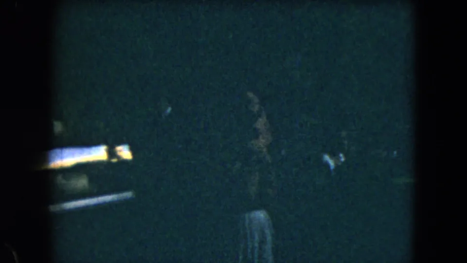 1962 Mexico City home-movie frame showing a partially visible person in a dim interior, with heavy grain and low exposure.
