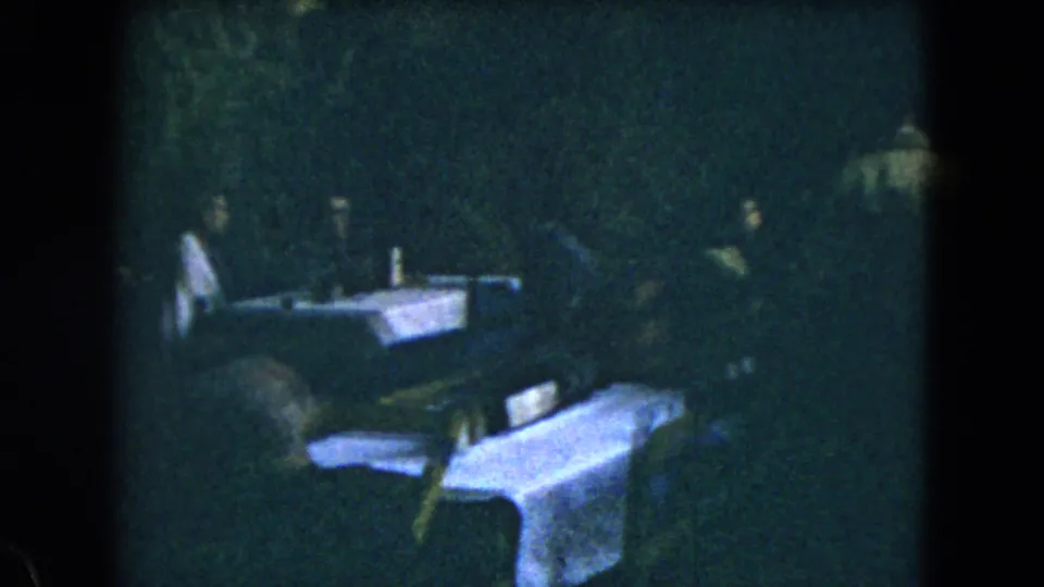 A 1962 Mexico City frame shows people gathered around white-covered tables, with chairs and table items visible in low light.