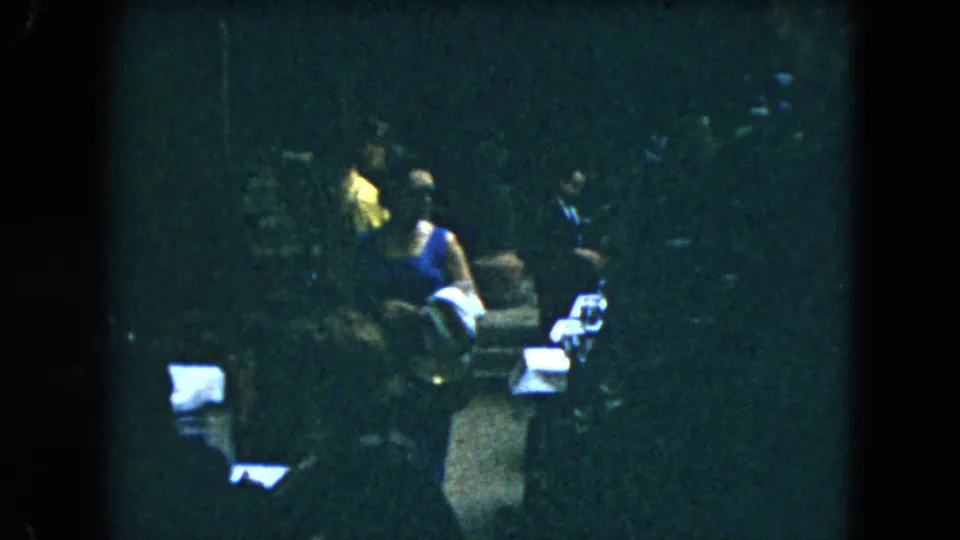 Home-movie frame from Mexico City in 1962 showing guests beside chairs and white-covered tables, including one figure in a yellow top.