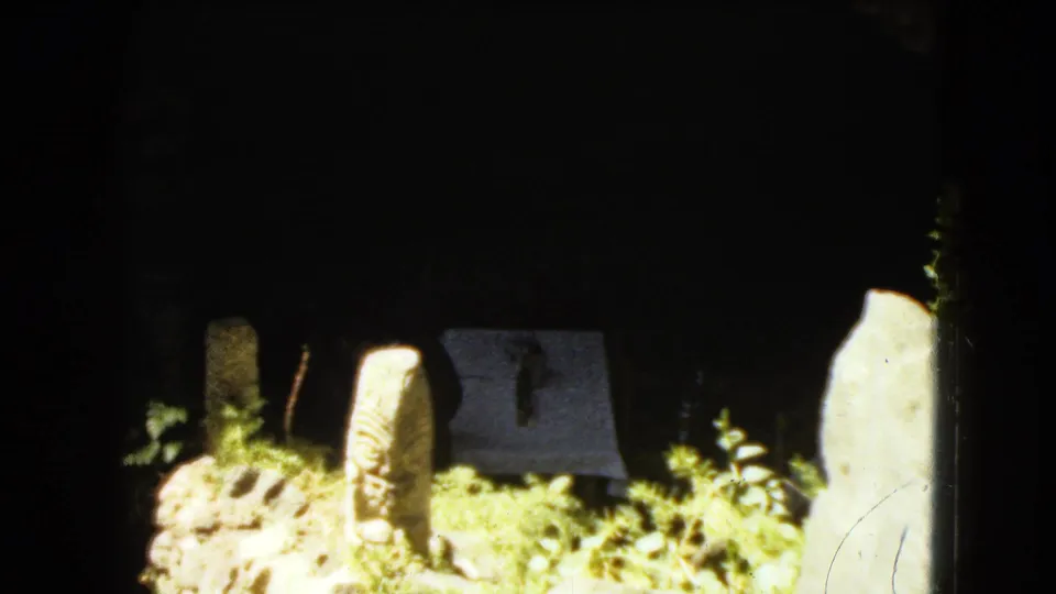 The final frame shows bright grass and stone markers before a dark masonry backdrop, with a pale covered display or marker near the center.