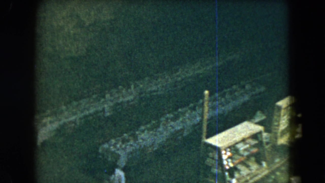 1962 Mexico City 8mm frame with dark film edges, rough stonework, and a partly visible sunlit ledge.