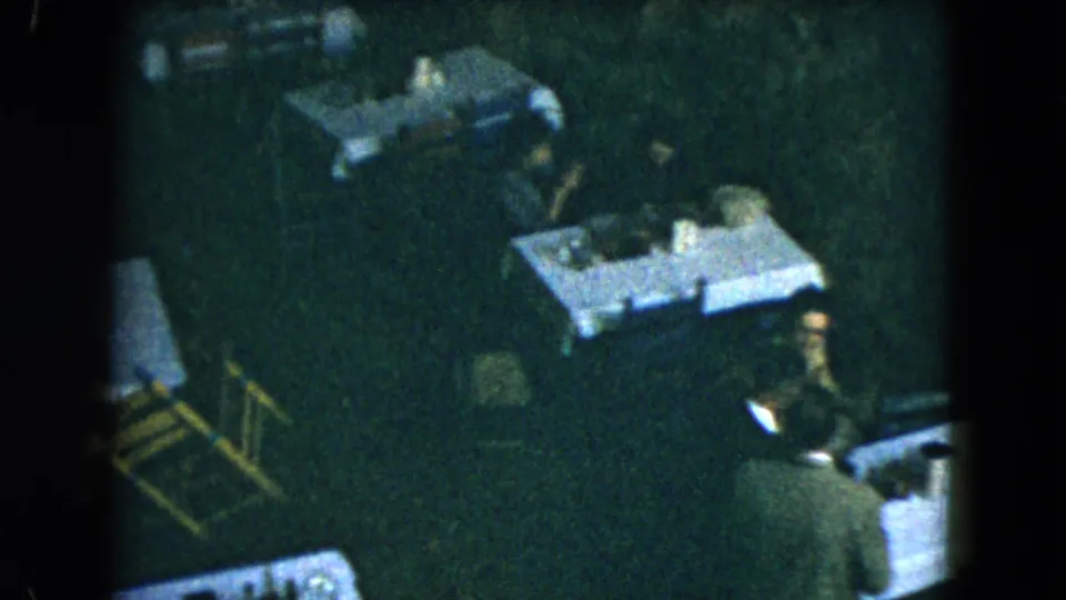 1962 Mexico City frame of workers arranging a dim restaurant dining room with white-covered tables.