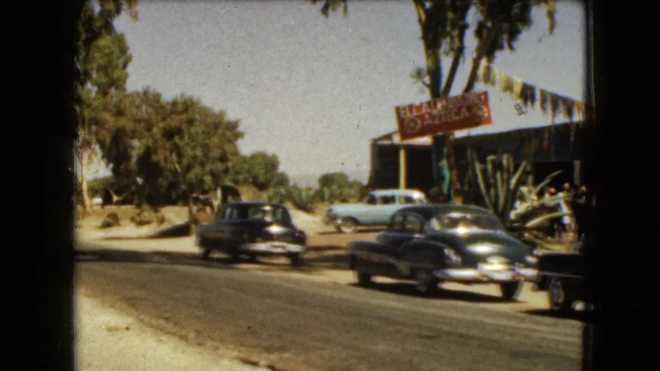 1962 Mexico City street view with classic cars passing an outdoor restaurant frontage marked by an El Azteca sign.