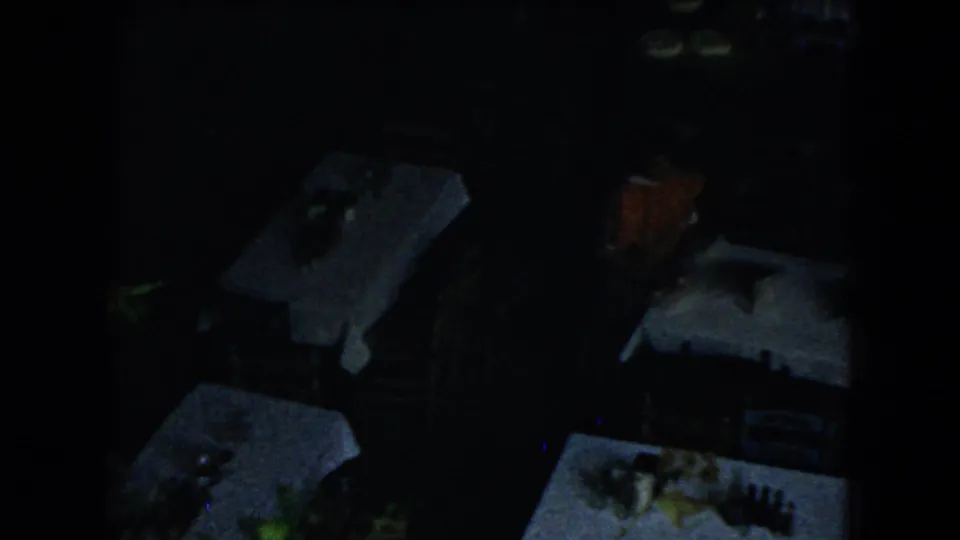 Dimly exposed 8mm view of a restaurant dining area with white tablecloths, chairs, and table settings.