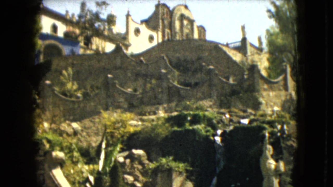 Arched stone or stucco structure below a church-like facade in bright daylight.