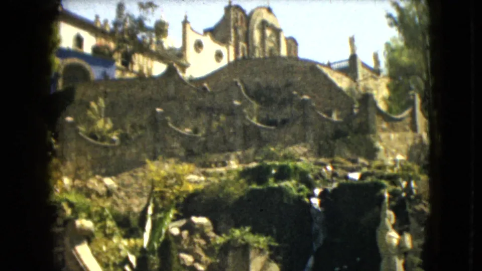 1962 Mexico City home-movie frame showing arched masonry and church-like architecture above garden foliage.