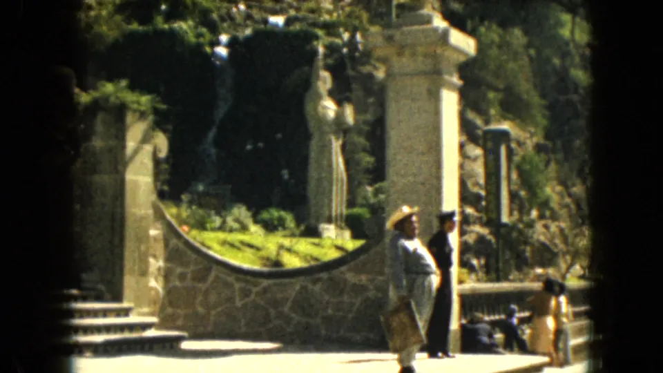 1962 Mexico City travel footage frame with visitors in period clothing near steps, stonework, waterfall, and a white statue.