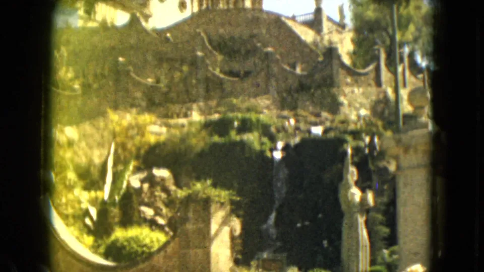1962 Mexico City home-movie frame emphasizing the man-made waterfall, white statue, stone wall, and garden plantings.