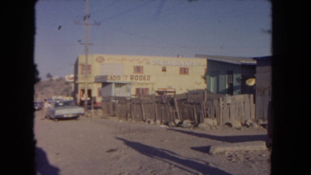 Yellow signed building beside a dirt road, parked sedan, wooden fence, and utility pole.