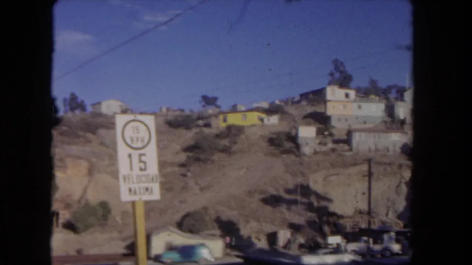 1962 Los Angeles hillside street view with a 15 MPH speed limit sign, houses, parked cars, trees, and overhead wire.