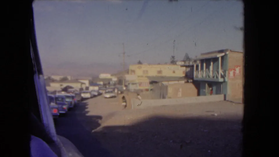 End frame of the 1962 Los Angeles moving-vehicle view, showing a pedestrian crossing near parked cars and low roadside buildings.