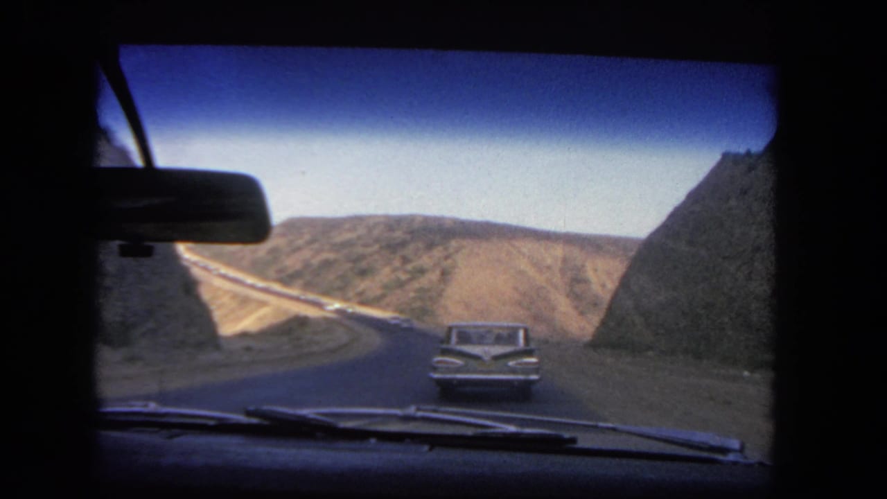 1962 Los Angeles home-movie windshield view of a sedan ahead on a hillside road, with dashboard and rearview mirror visible.