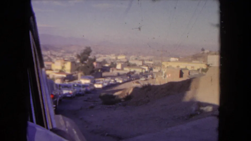 Los Angeles home-movie view from a car window toward a distant cityscape and traffic at the base of dry hills in 1962.