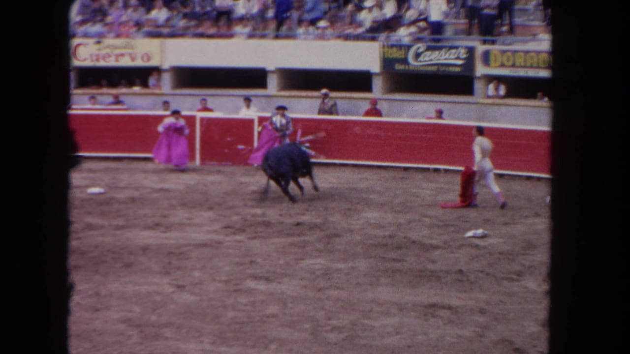 1962 Los Angeles 8mm frame showing a matador with a pink cape as a black bull turns across a dusty arena.