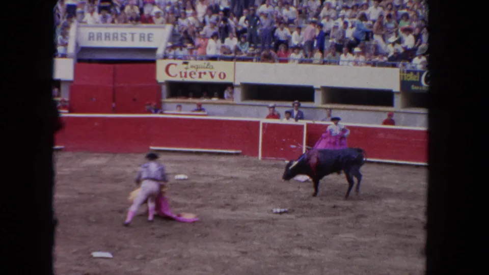 1962 Los Angeles 8mm frame showing a black bull moving past a matador low on the dusty arena floor.