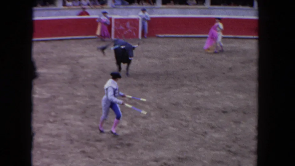 1962 Los Angeles 8mm frame showing a matador carrying banderillas while the black bull stands in the arena near performers with pink capes.