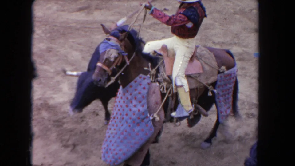 1962 Los Angeles 8mm frame showing a mounted rider controlling a decorated horse near a black bull during the arena event.