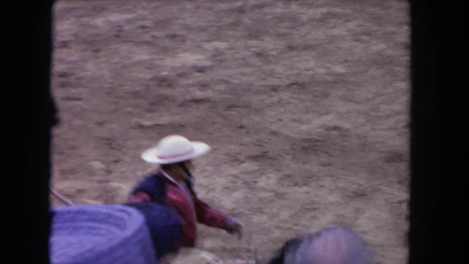 Obstructed 1962 Los Angeles home-movie view of the mounted rider passing below the spectator area in the sandy arena.