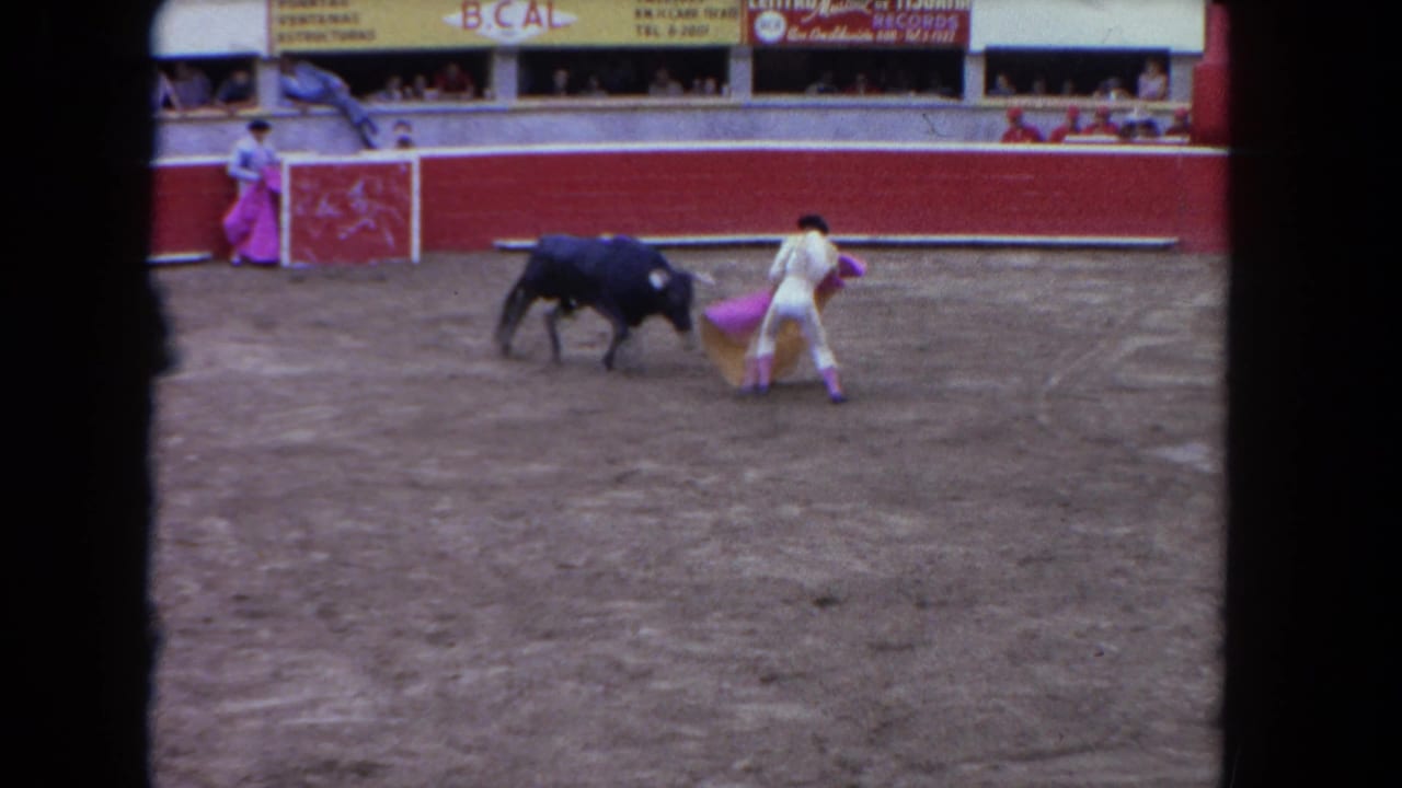 1962 Los Angeles 8mm frame showing a matador in a pale suit confronting a dark bull with a pink cape in an arena.