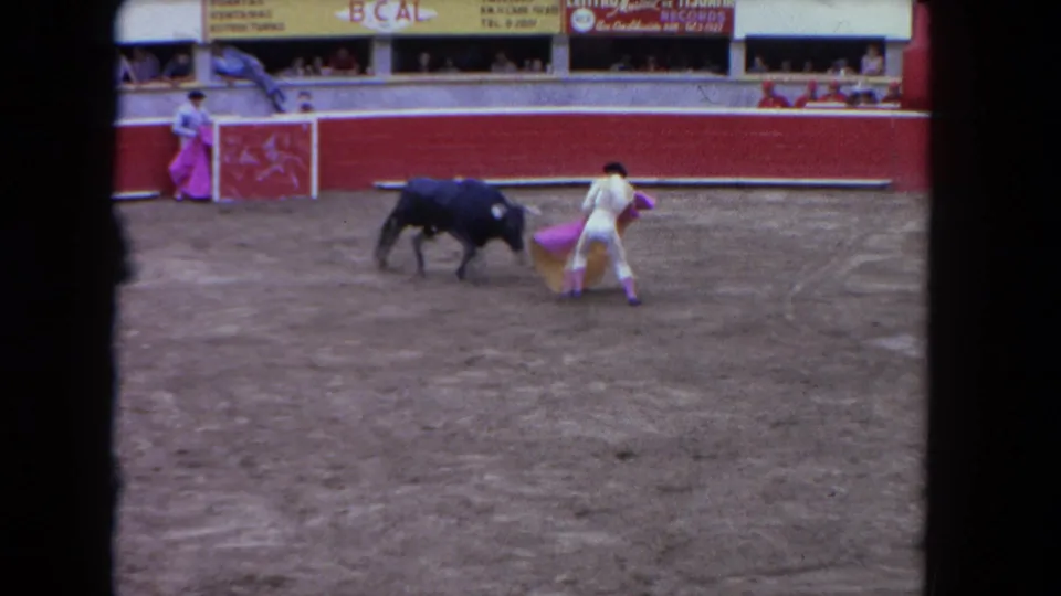 1962 Los Angeles 8mm frame showing a matador in a pale suit confronting a dark bull with a pink cape in an arena.