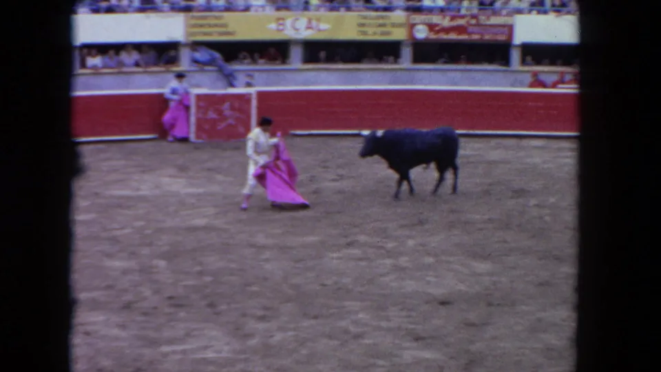 1962 Los Angeles 8mm frame of a matador holding a pink cape while a dark bull moves away in the sandy arena.