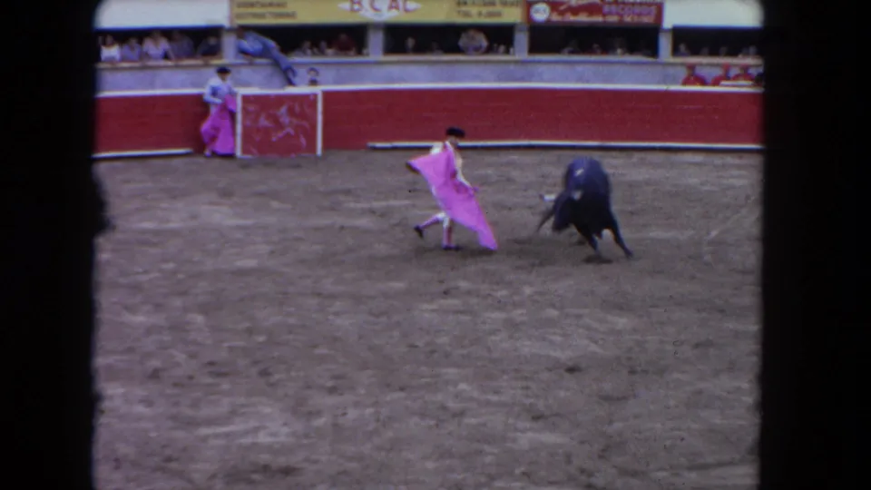 1962 Los Angeles 8mm frame showing the black bull lunging as the matador sweeps a pink cape in the arena.