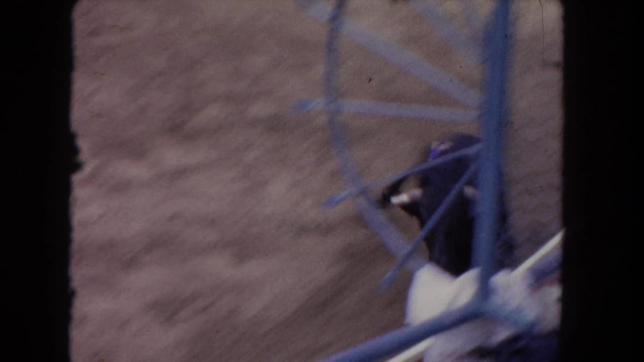 1962 Los Angeles 8mm frame showing a black bull partly hidden behind dark foreground framing and blue railings in a dirt arena.