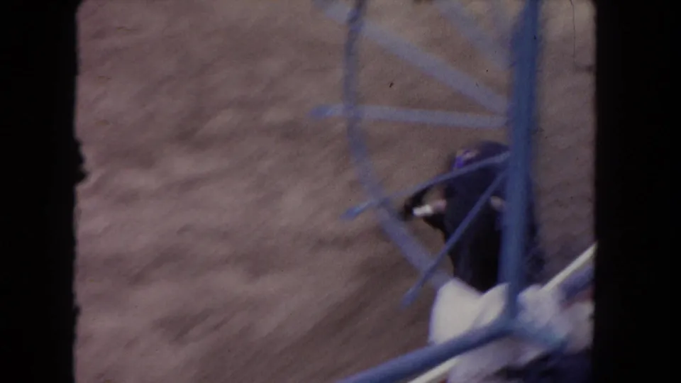 1962 Los Angeles 8mm frame showing a black bull partly hidden behind dark foreground framing and blue railings in a dirt arena.