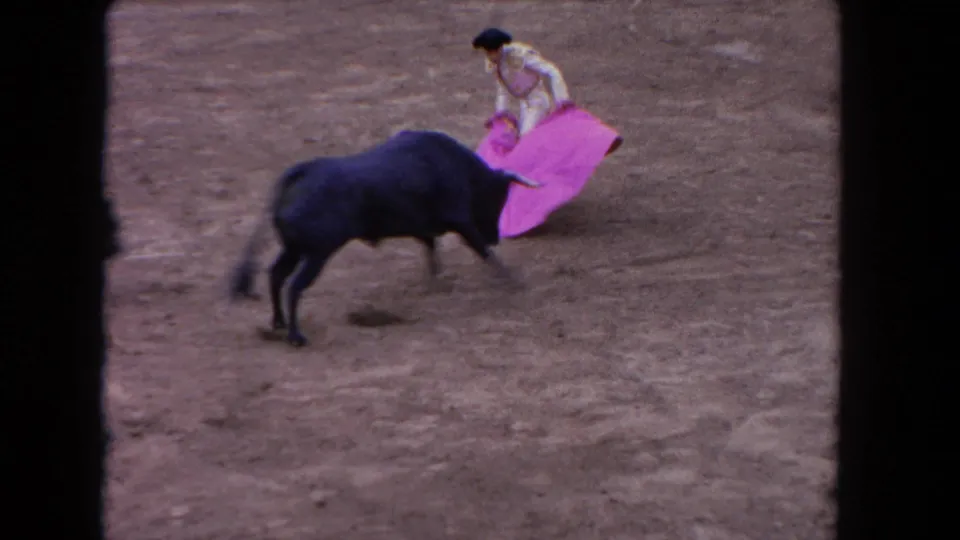 1962 Los Angeles bullfight frame with a matador in white guiding a bright pink cape as a black bull approaches on the dirt ring.