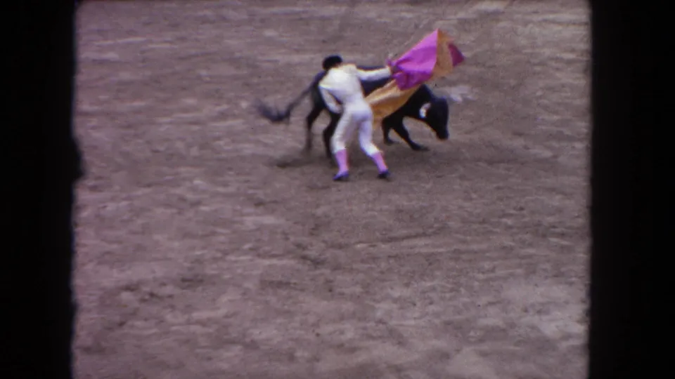 1962 Los Angeles 8mm frame showing the matador turning with the cape as the black bull passes close on the arena floor.