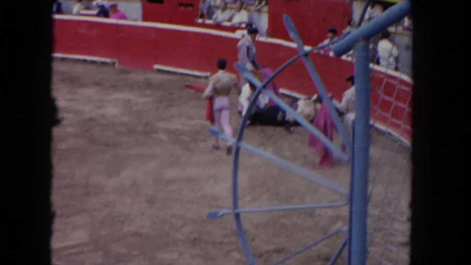 1962 Los Angeles 8mm frame showing a matador with a pink cape near a black bull at the edge of the arena, with spectators above the wall.