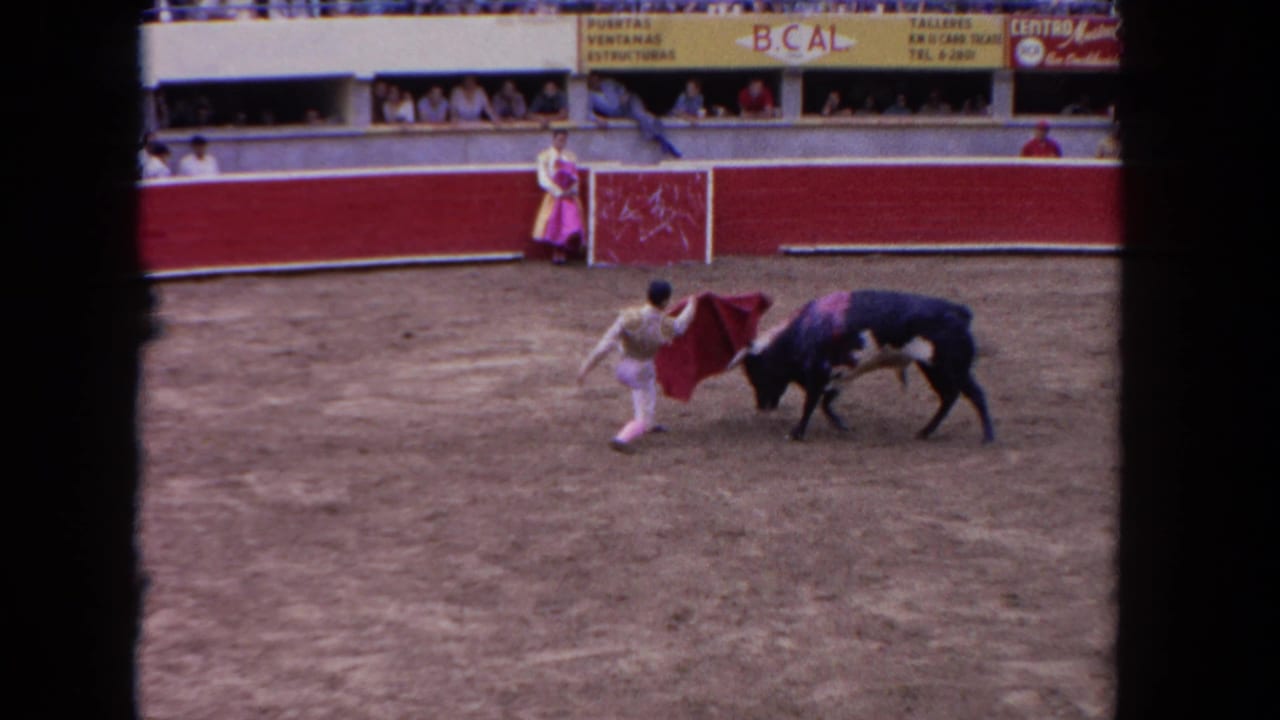 Matador crouches with a red cape as a black bull approaches in a dusty arena.