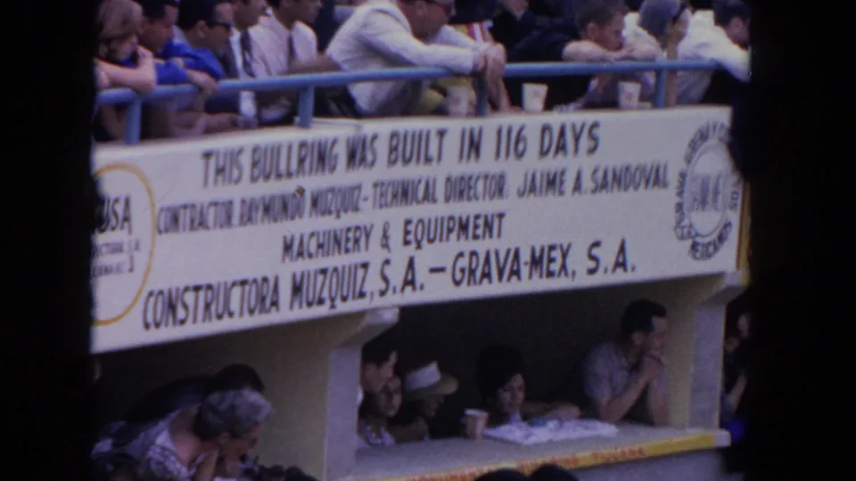 1962 Los Angeles home-movie frame showing spectators around a bullring banner crediting construction personnel and companies.