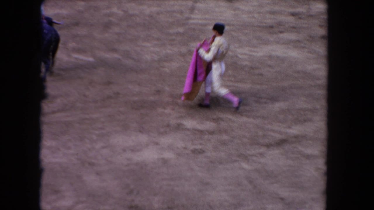 In 1962 Los Angeles home-movie footage, a matador in a light costume carries a pink cape across a dusty arena.