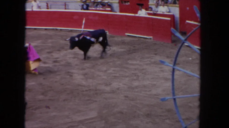 A matador with a pink cape faces a dark bull in the Los Angeles bullfighting-style arena, filmed on 8mm in 1962.