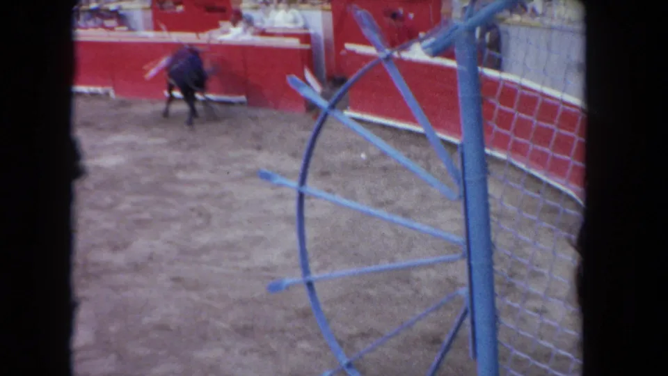 1962 Los Angeles arena frame with a black bull near the red wall, partly obscured by a blue metal foreground structure.