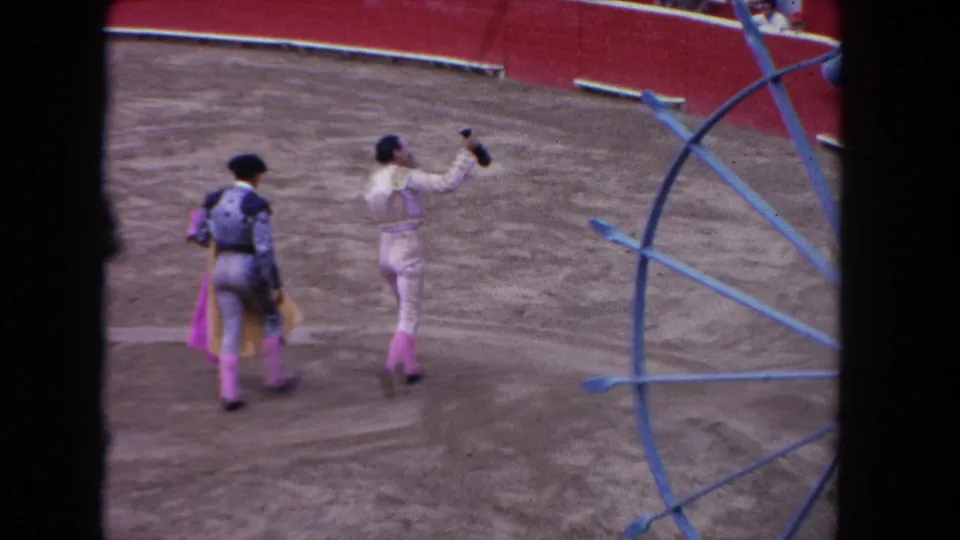 1962 Los Angeles bullfighting-style arena frame with two matadors walking near blue metal equipment and a red barrier.