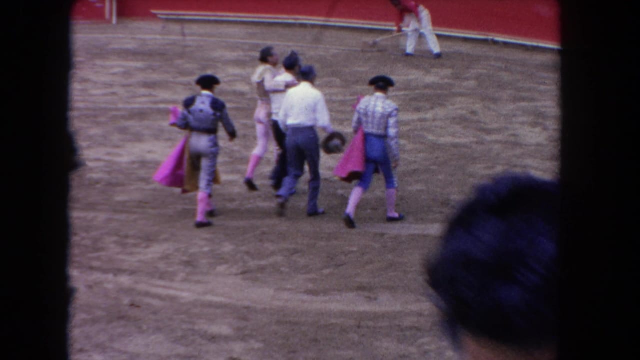 Matadors and attendants walk across a sandy arena beside a red barrier.