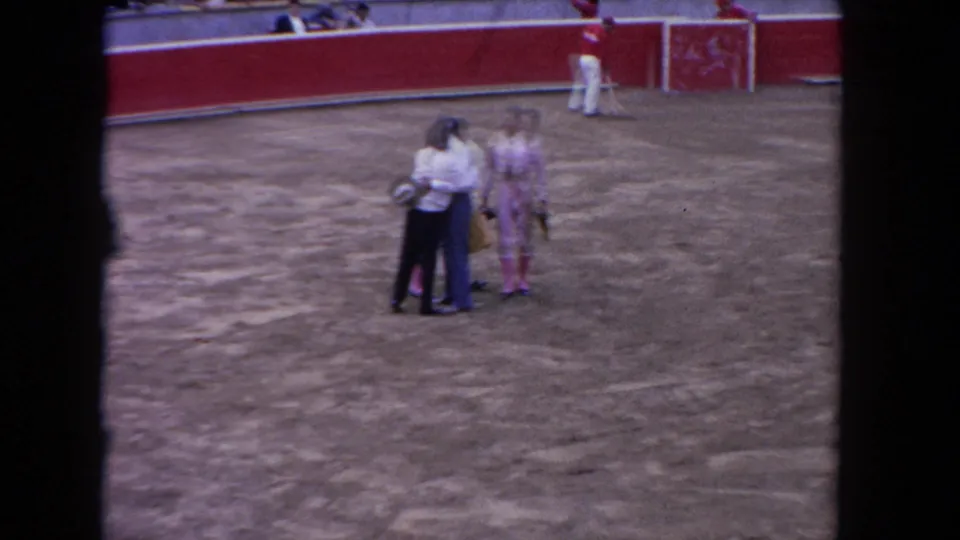 1962 Los Angeles bullring frame showing matadors and attendants gathered on the arena floor, with a red wall and staff behind them.