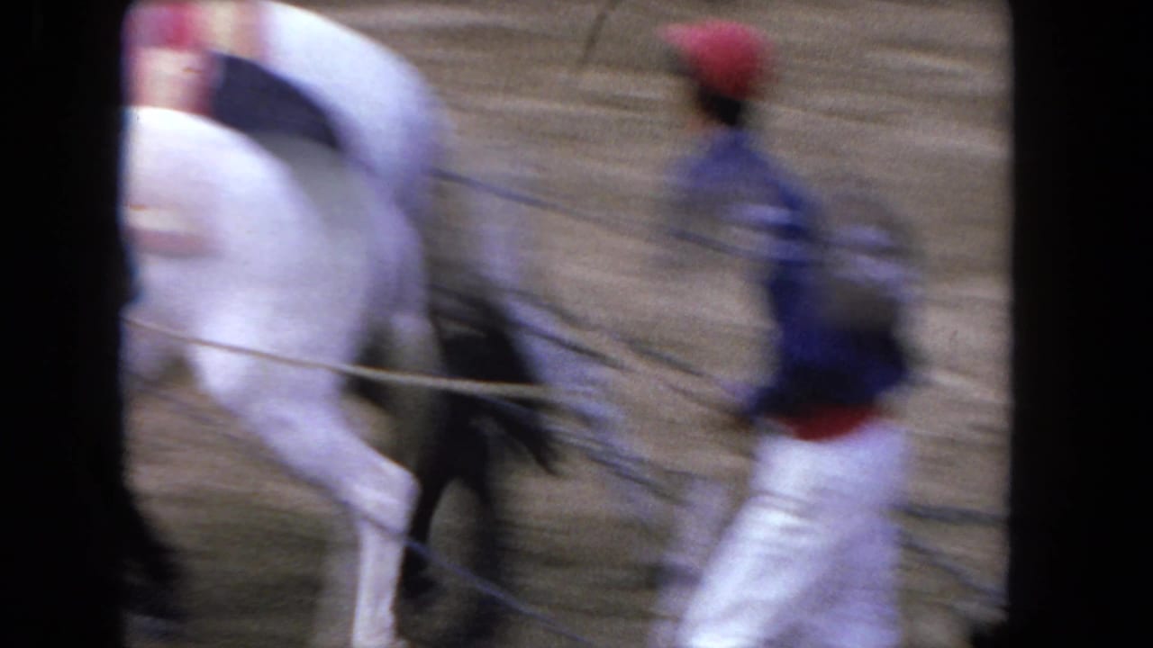 Blurred 1962 Los Angeles 8mm frame showing men moving near an apparent bull on a sandy bullfighting ring floor.