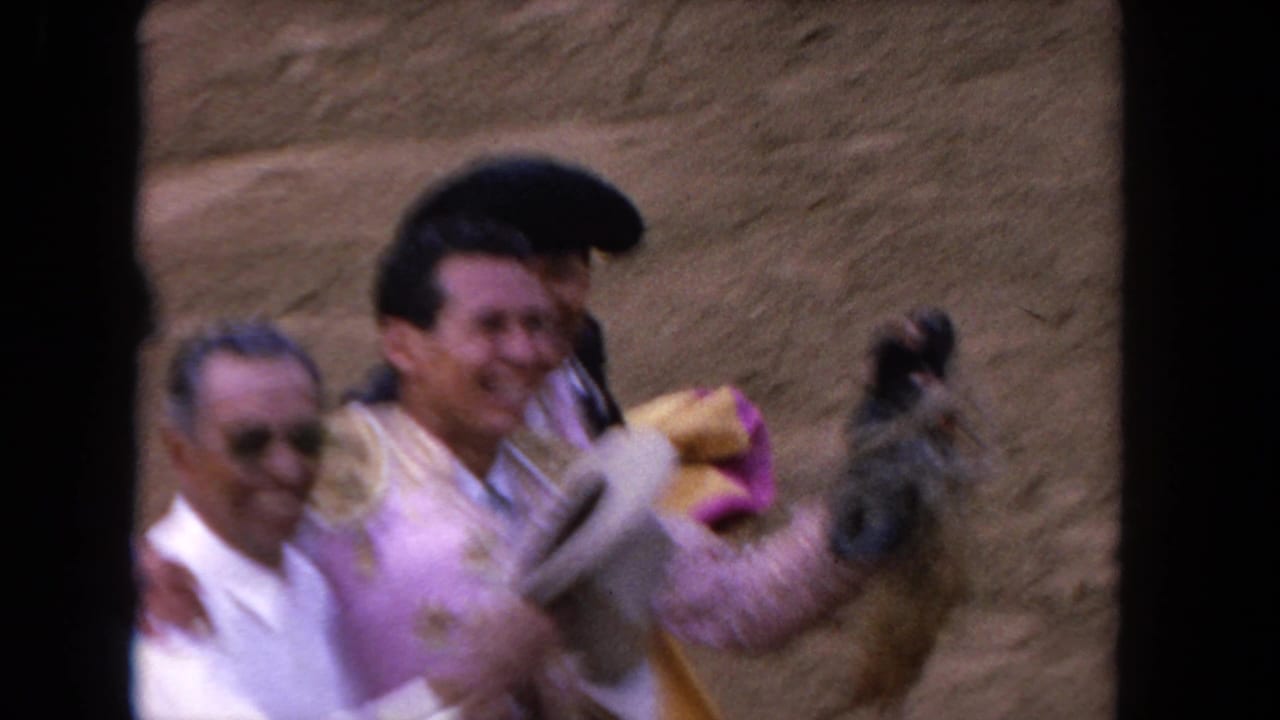 Matador in pink and gold beside men in white on a sandy arena.