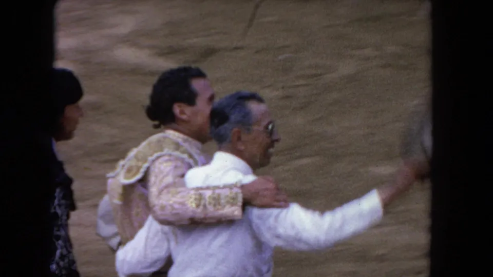 1962 Los Angeles 8mm frame showing the matador walking arm-in-arm with a man in white during the arena celebration.