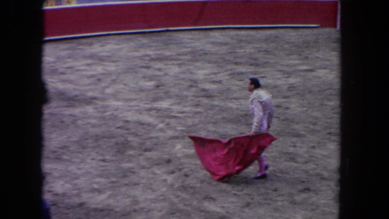 Bullfighter walking across a sandy ring while holding a red cape.